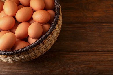 Raw chicken eggs in wicker basket on wooden table, space for text