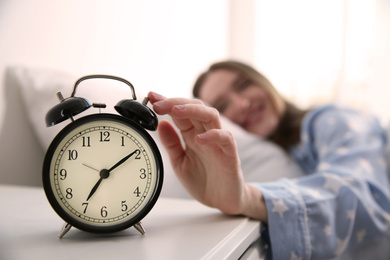 Young woman turning off alarm clock at home in morning, focus on hand