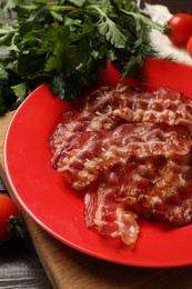 Photo of Plate with fried bacon slices, tomatoes and parsley on table, closeup