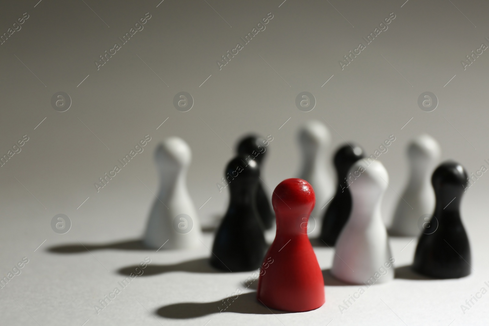 Photo of Red game piece among black and white ones on light grey background, closeup. Career promotion concept