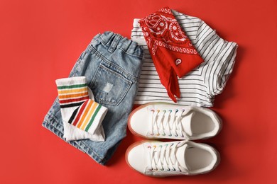 Stylish child clothes, shoes and accessories on red background, flat lay