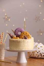 Photo of Delicious cake decorated with sweets and burning candle on wooden table