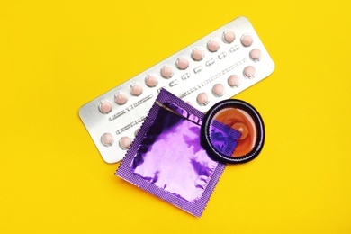 Photo of Condoms and birth control pills on yellow background, flat lay. Safe sex concept