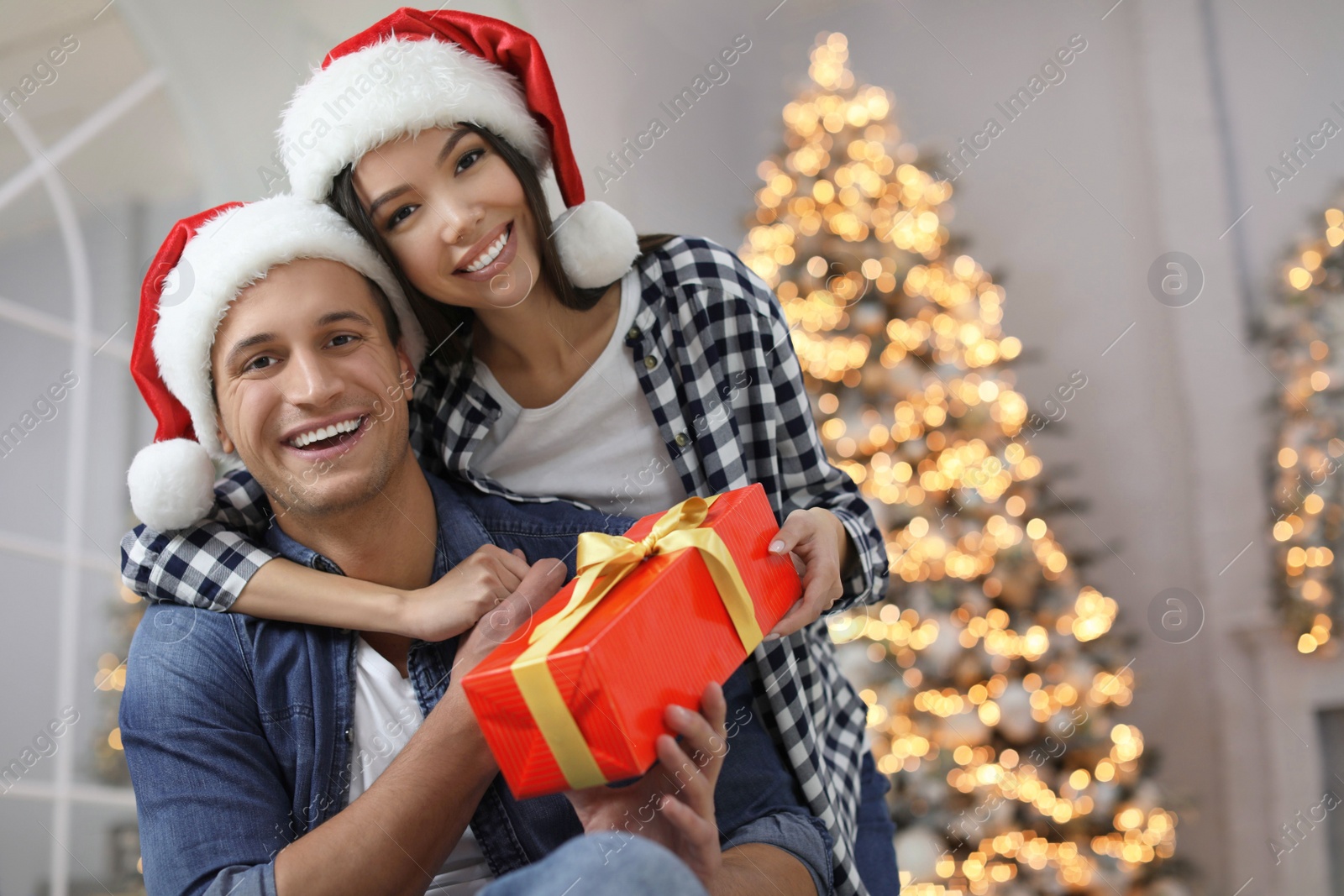 Photo of Happy young couple in Santa hats with Christmas gift at home