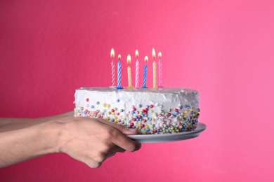 Photo of Woman holding birthday cake with burning candles on pink background, closeup