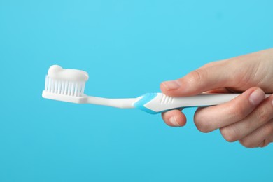 Photo of Woman holding toothbrush with paste on light blue background, closeup