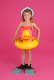Cute little child in beachwear with bright inflatable ring on pink background