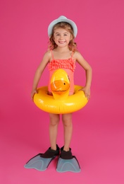 Photo of Cute little child in beachwear with bright inflatable ring on pink background