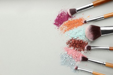 Makeup brushes and scattered eye shadows on light grey background, flat lay. Space for text