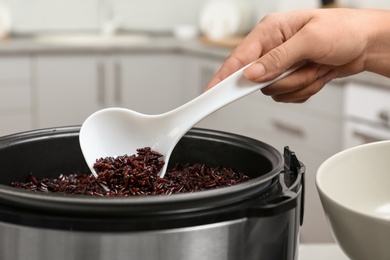 Photo of Woman putting brown rice into bowl from multi cooker in kitchen, closeup
