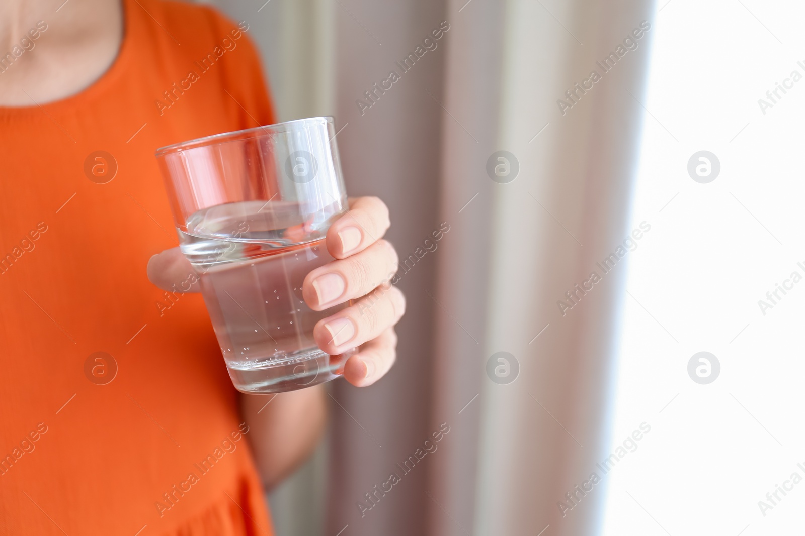 Photo of Woman holding glass of water near window at home, closeup