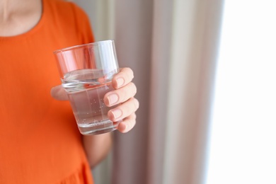 Photo of Woman holding glass of water near window at home, closeup