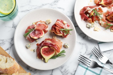 Delicious ripe figs and prosciutto served on white marble table, flat lay