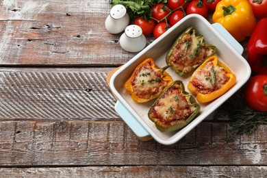 Photo of Tasty stuffed peppers in dish and ingredients on wooden table, flat lay. Space for text