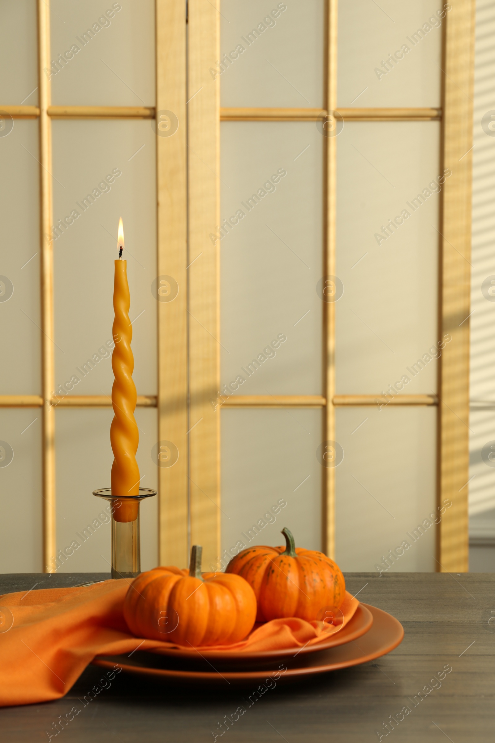 Photo of Burning candle and fresh pumpkins on wooden table indoors