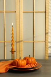 Burning candle and fresh pumpkins on wooden table indoors