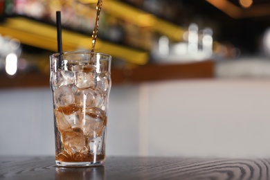 Pouring cola into glass with ice cubes on table indoors. Space for text