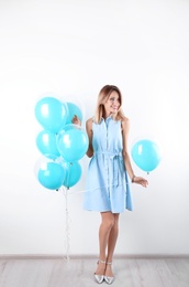 Young woman with air balloons near white wall