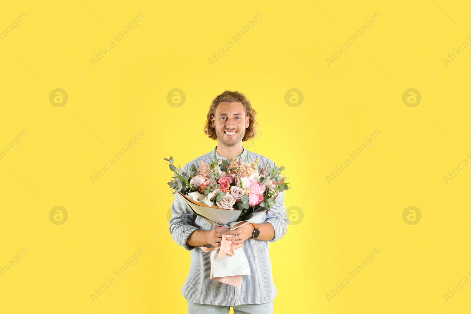 Photo of Young handsome man with beautiful flower bouquet on yellow background