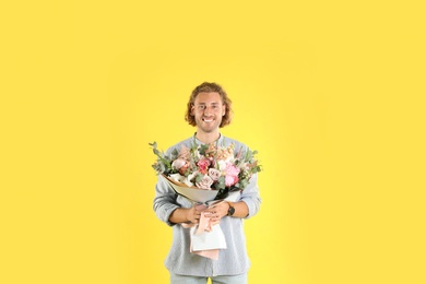 Young handsome man with beautiful flower bouquet on yellow background