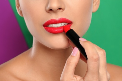 Young woman applying lipstick on color background, closeup