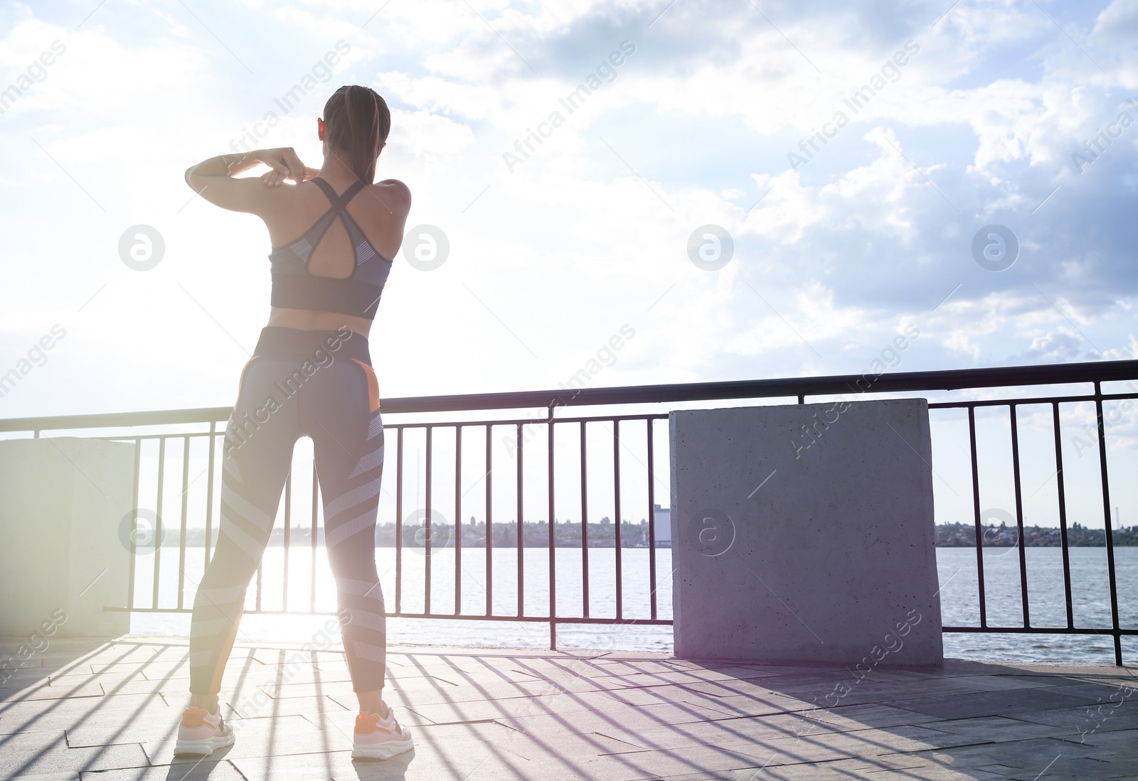 Photo of Young woman stretching on pier near river in morning, back view. Space for text