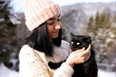 Photo of Happy young woman with black cat outdoors on winter day