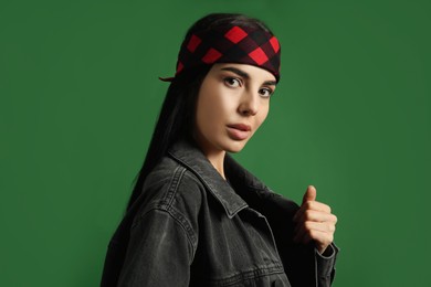 Photo of Fashionable young woman in stylish outfit with bandana on green background