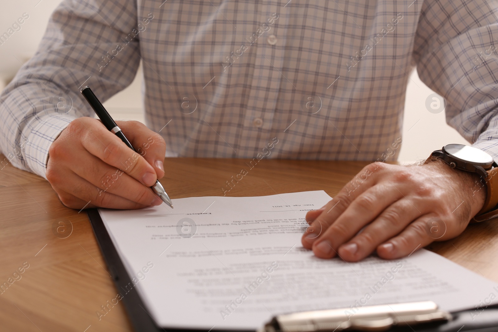 Photo of Businessman signing contract at wooden table, closeup of hands