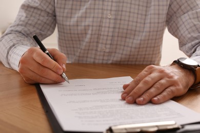 Businessman signing contract at wooden table, closeup of hands