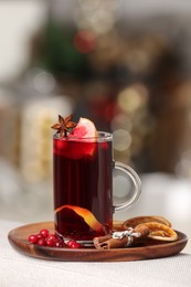 Aromatic mulled wine in cup and ingredients on sofa armrest against blurred background