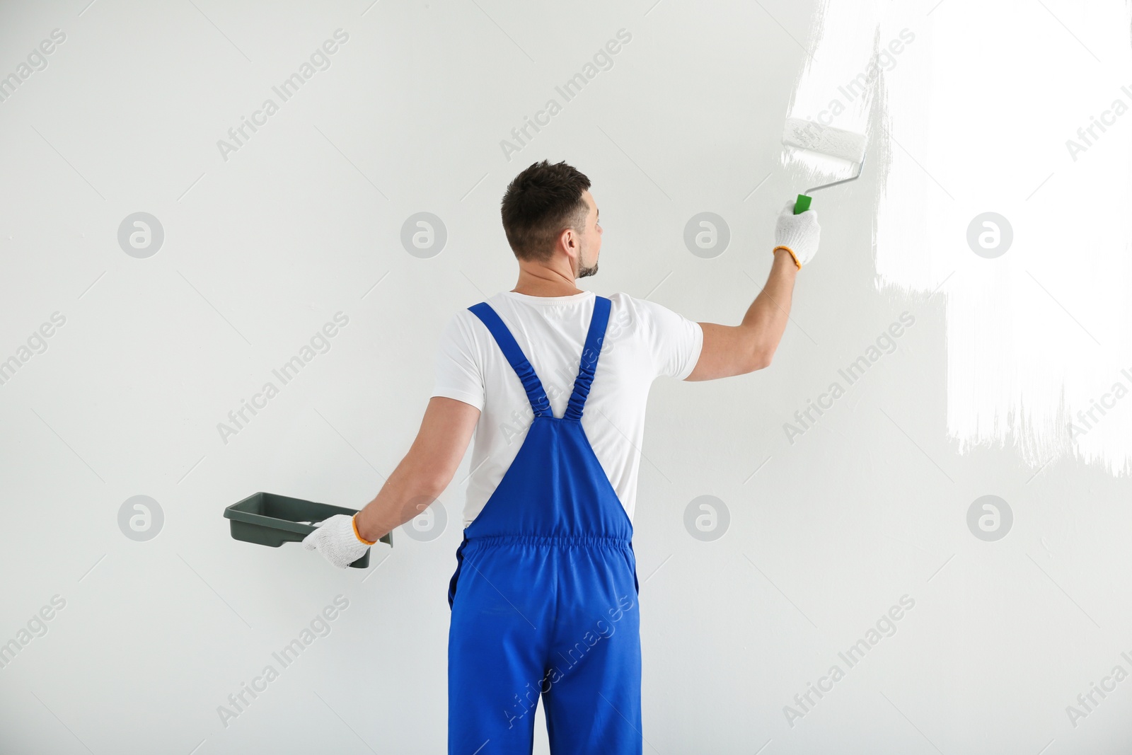 Image of Man painting wall with white dye indoors, back view