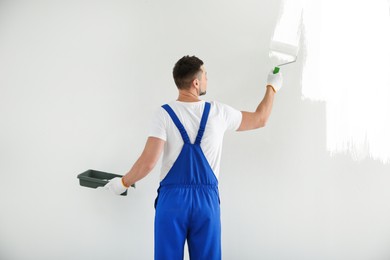 Man painting wall with white dye indoors, back view