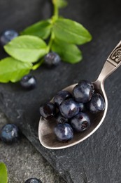 Photo of Spoon with tasty fresh bilberries on dark grey table, closeup