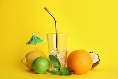 Photo of Glass with ice and straw surrounded by ingredients for summer cocktail on color background