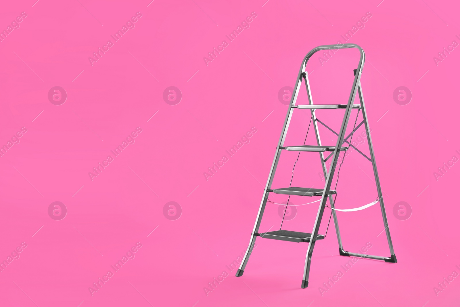 Photo of Modern metal stepladder on pink background. Space for text