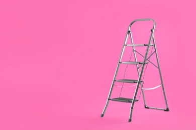 Photo of Modern metal stepladder on pink background. Space for text