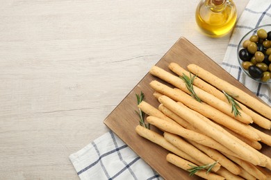 Delicious grissini sticks, rosemary, oil and olives on wooden table, flat lay. Space for text