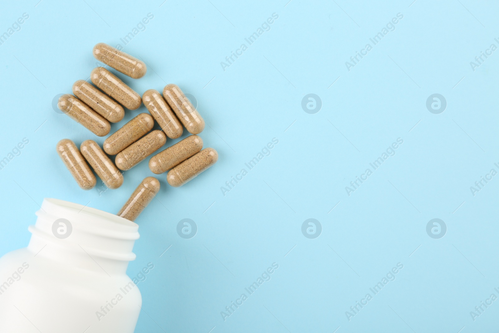 Photo of Bottle and vitamin capsules on light blue background, top view. Space for text