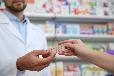 Photo of Professional pharmacist giving pills to customer in drugstore, closeup