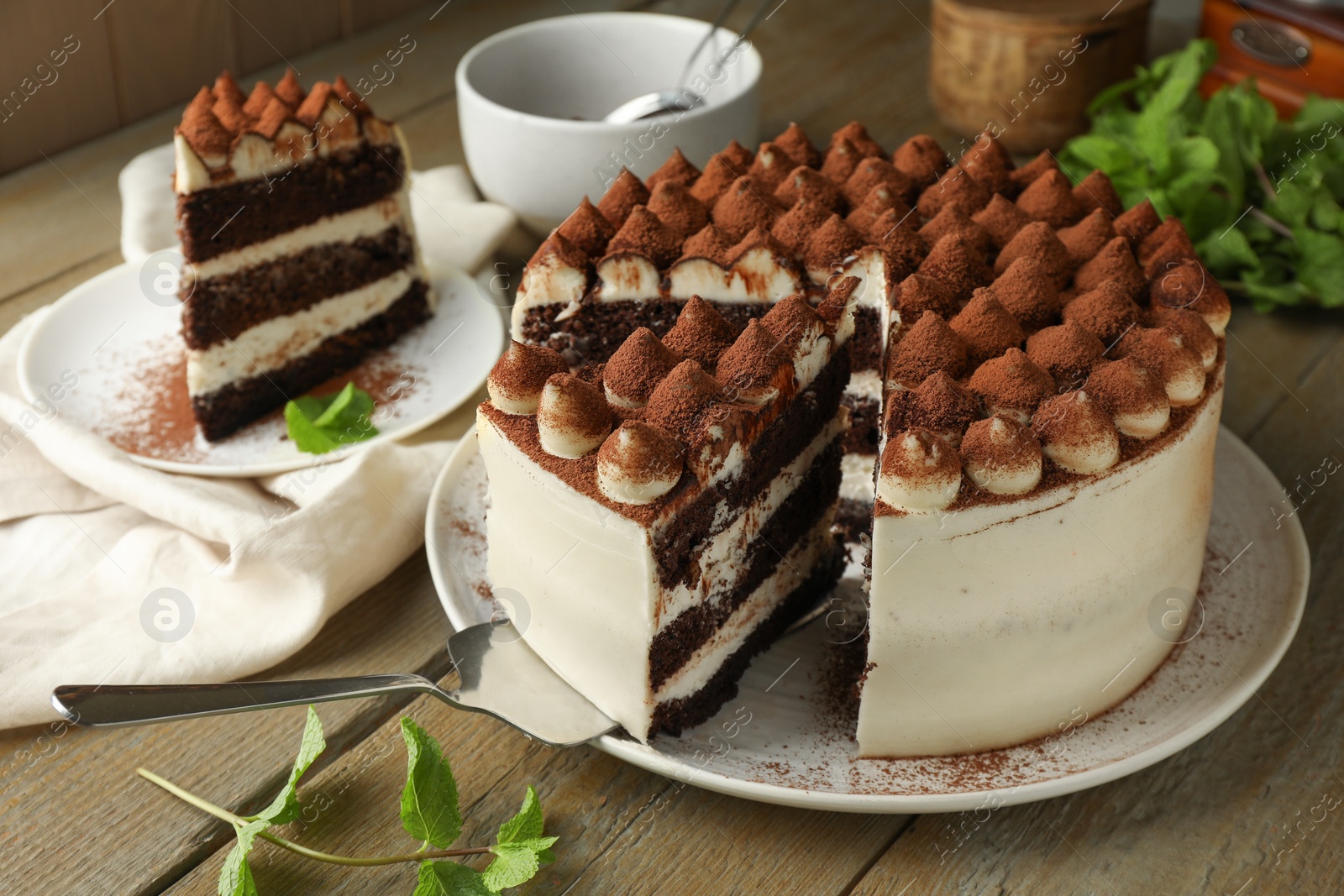 Photo of Delicious tiramisu cake with mint leaves and server on wooden table