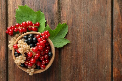 Photo of Different fresh ripe currants and green leaves on wooden table, flat lay. Space for text