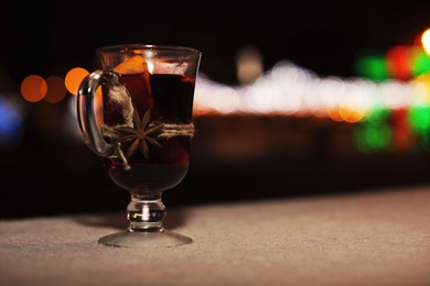 Glass cup of mulled wine on table against blurred background. Space for text