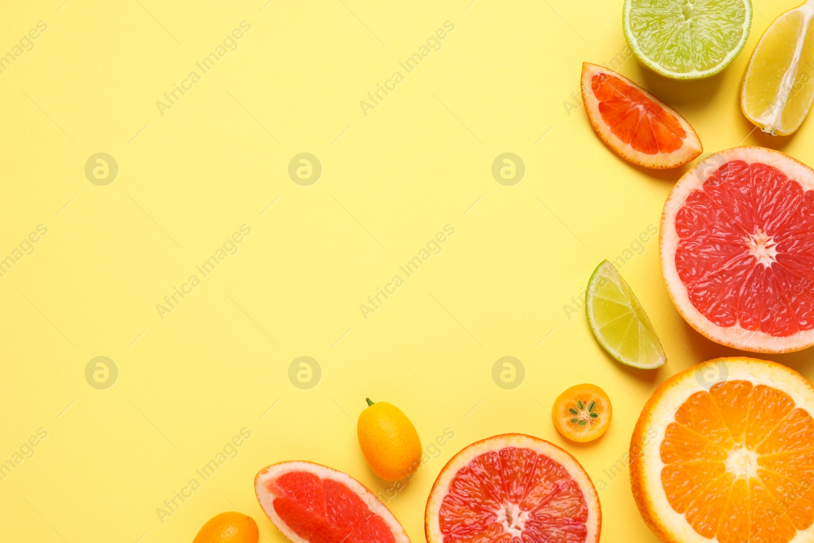 Photo of Fresh juicy citrus fruits on light yellow background, flat lay. Space for text