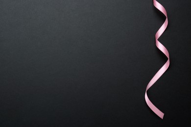 Beautiful pink ribbon on black background, top view. Space for text