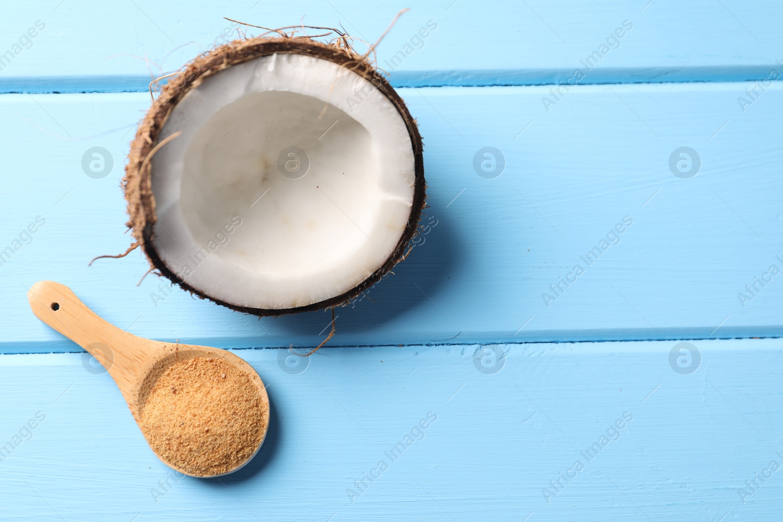 Photo of Spoon with coconut sugar and half of fruit on light blue wooden table, top view. Space for text