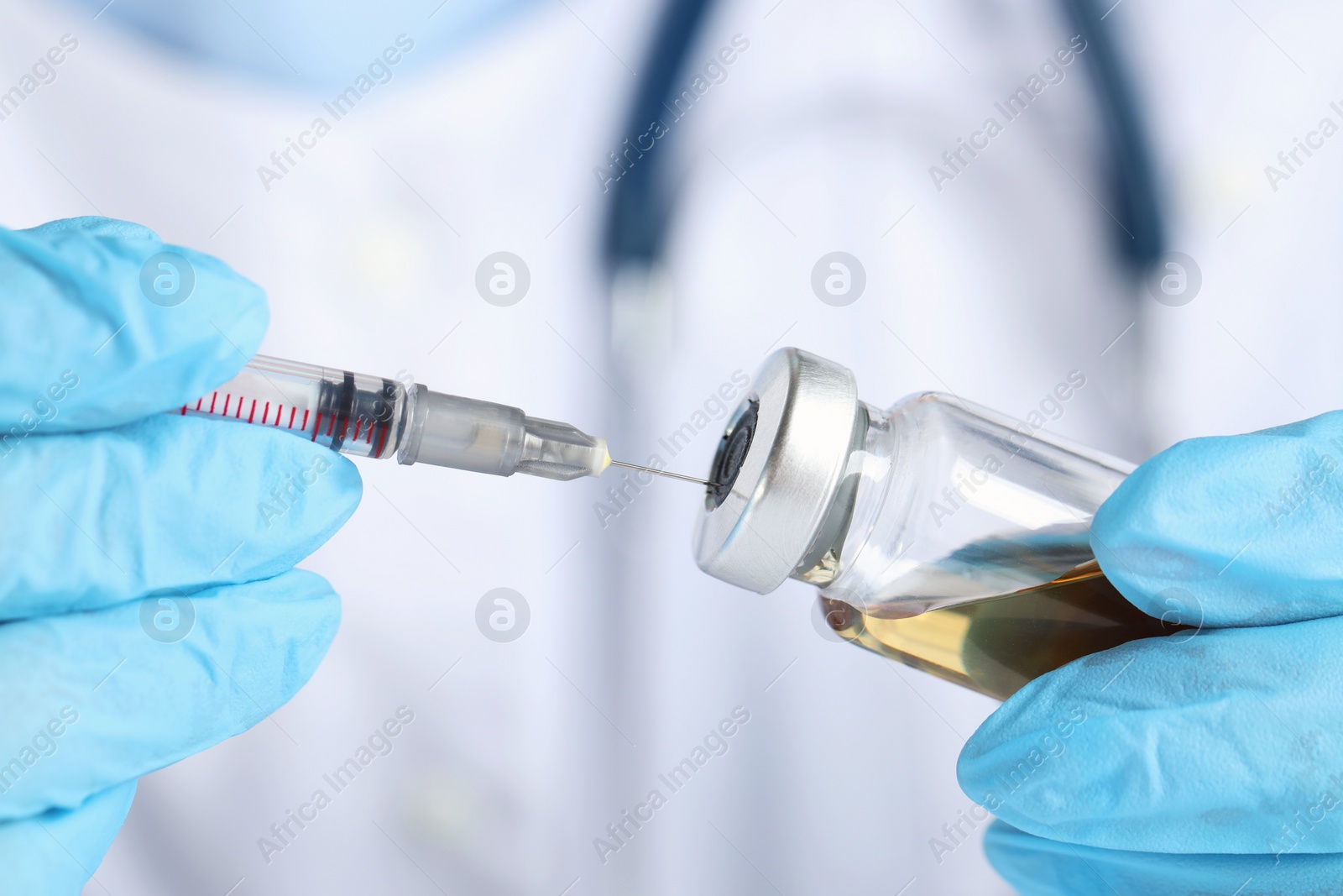 Photo of Doctor inserting syringe into glass vial with medication, closeup