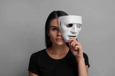 Multiple personality concept. Woman with mask on grey background