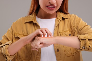Photo of Suffering from allergy. Young woman scratching her arm on grey background, closeup