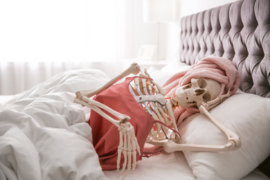 Photo of Human skeleton in silk pajamas and towel lying on bed indoors